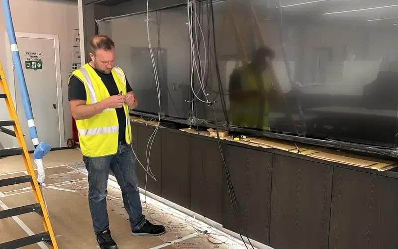 Engineer in a high-visibility vest surveying a wall of displays during a fit-out